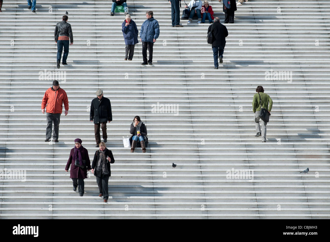 Some people climb steps of the Grande Arche of La Défense in Paris, France, while a woman eats her lunch. Stock Photo