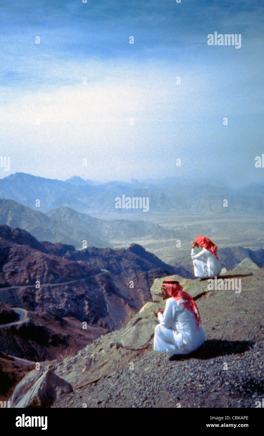 Saudi Arabia Hijaz Mountains Men Looking into Valley wearing Thobes and Red and White Shemagh Stock Photo