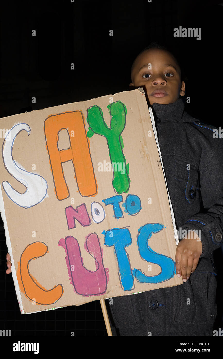 Young black boy holds a placard with colorful lettering that reads 'Say no to cuts' Stock Photo