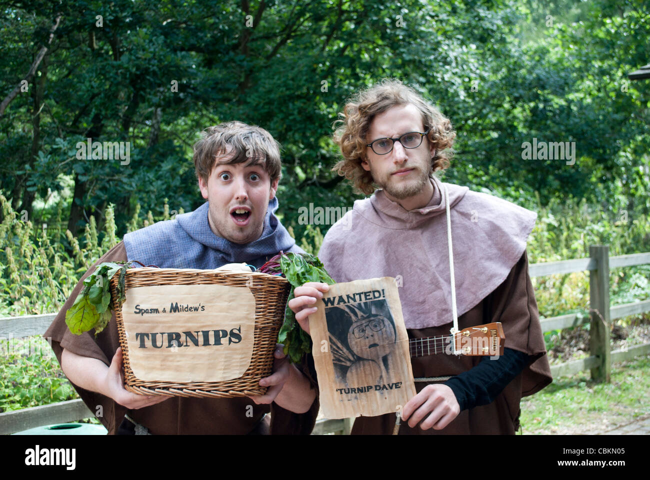 Two medieval peasants holding up a wicker basket with 'Spasm & Mildew's Turnips' sign and a flier with 'Wanted Turnip Dave' Stock Photo