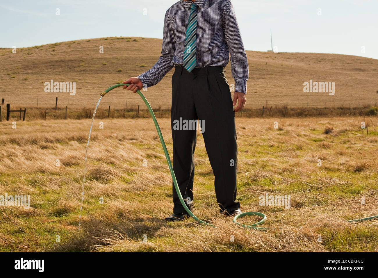 Man holding hose pipe in arid landscape Stock Photo