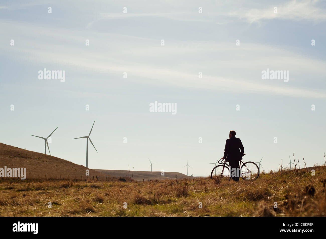 Distant view of man by bicycle watching wind farm Stock Photo