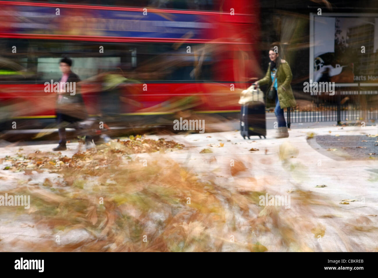 people caught in a gust of wind with leaves swirling around and a bus passing Stock Photo