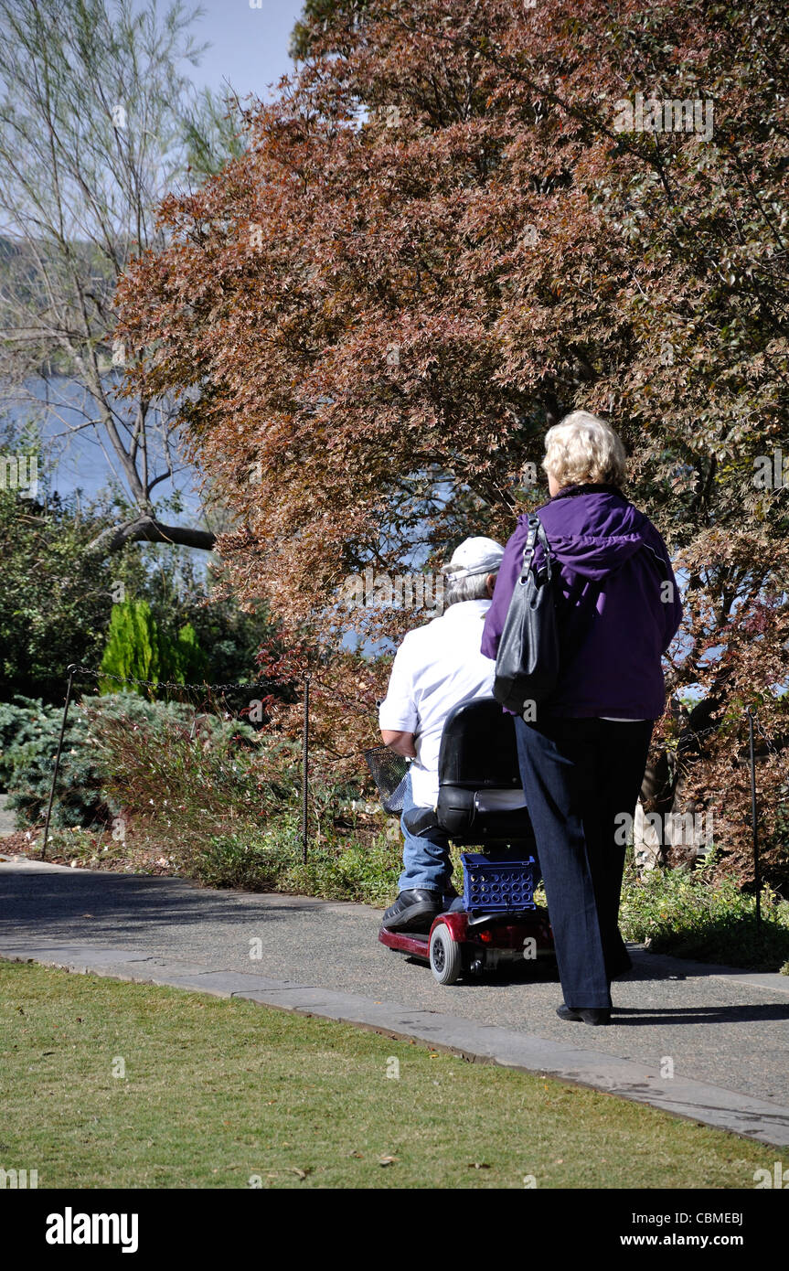 Handicapped elderly man in wheelchair and elderly woman accompanying him on a walk in park Stock Photo