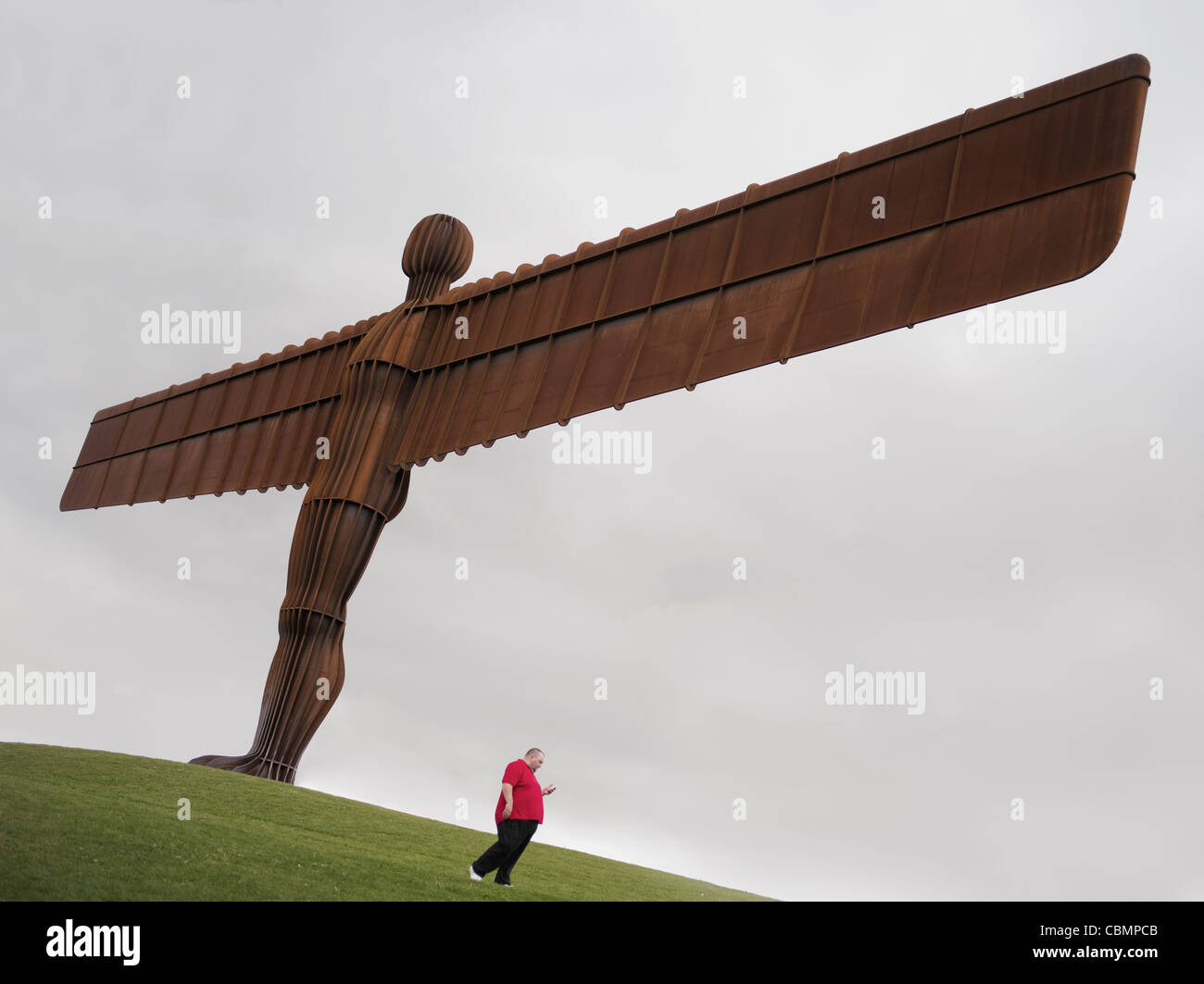 A tall lean Angel of the North  by Antony Gormley,  located in Gateshead, Tyne and Wear, England. Beneath an overweight man. Stock Photo