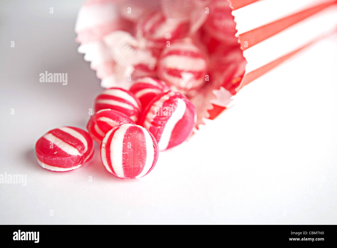 Red and white striped mint sweets spilling out of a paper bag Stock Photo