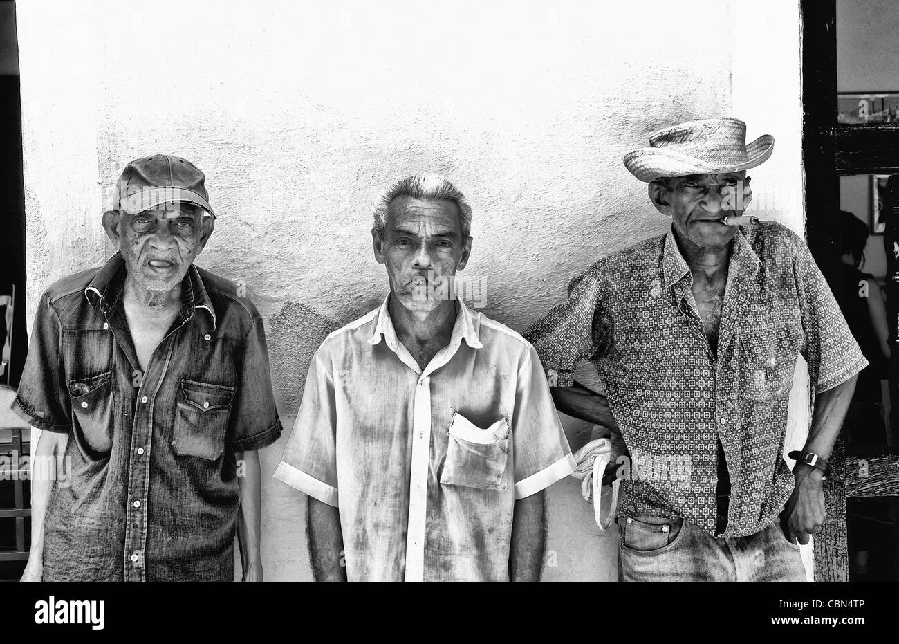 Local old men with cigar against bright yellow wall of building of the old colonial city of Trinidad in Cuba Stock Photo