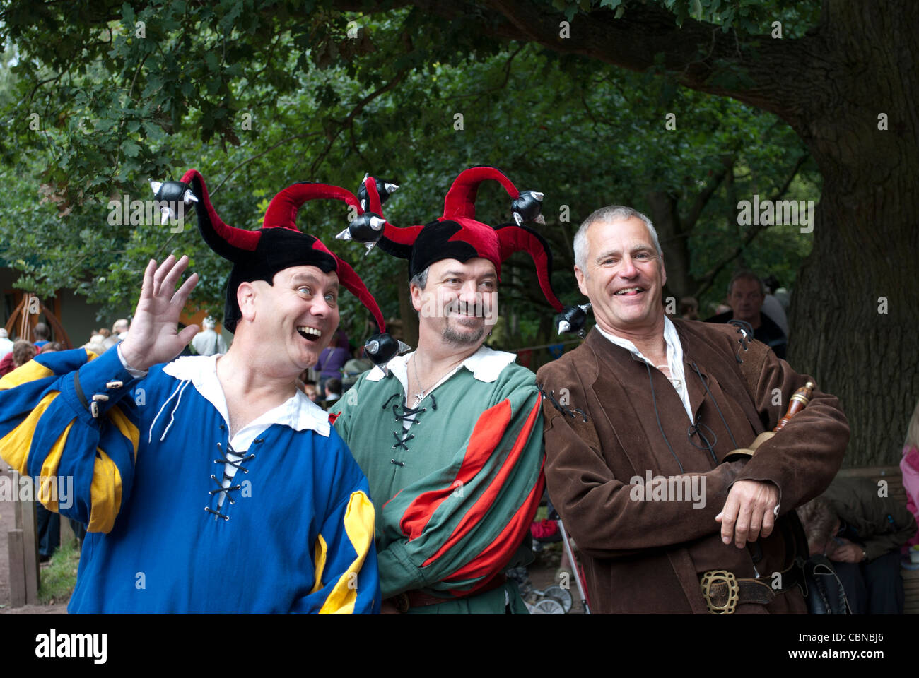 Three men in medieval clothing, two with jester hats on, smiling and laughing and waving at the Robin Hood festival Stock Photo