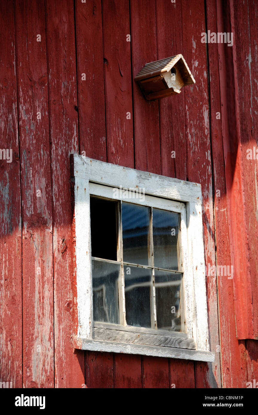 A birdhouse attached to the side of a barn over an old wooden window