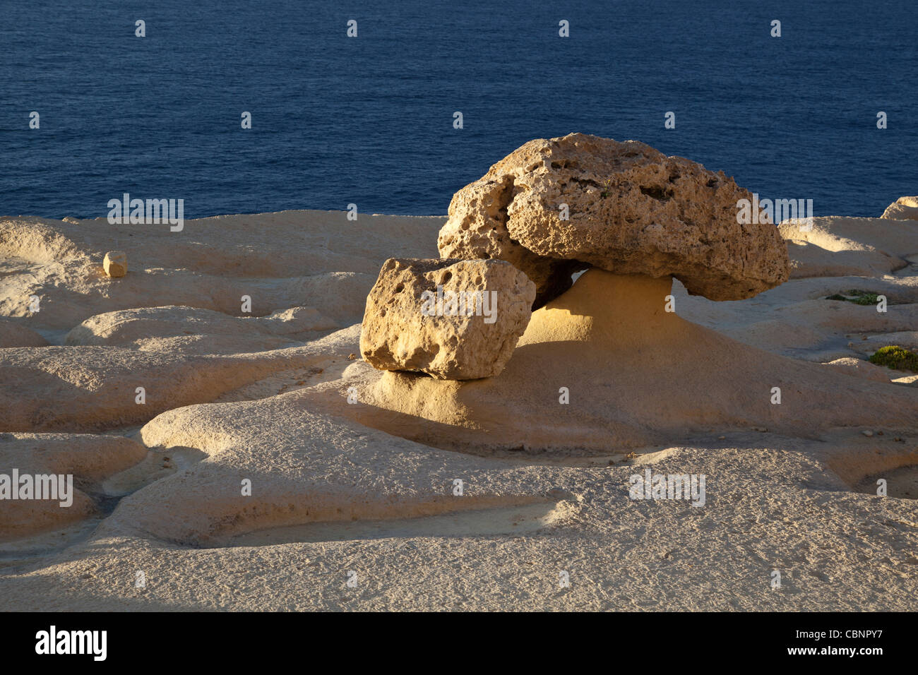 A boulder of hard stone left stranded as the softer limestone rocky layer underneath is eroded away with wind & water in Malta. Stock Photo
