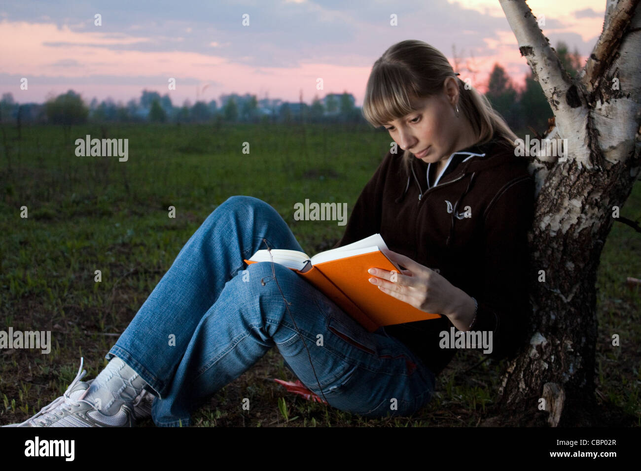 girl reading book and sitting outdoor under the tree with sky in ...