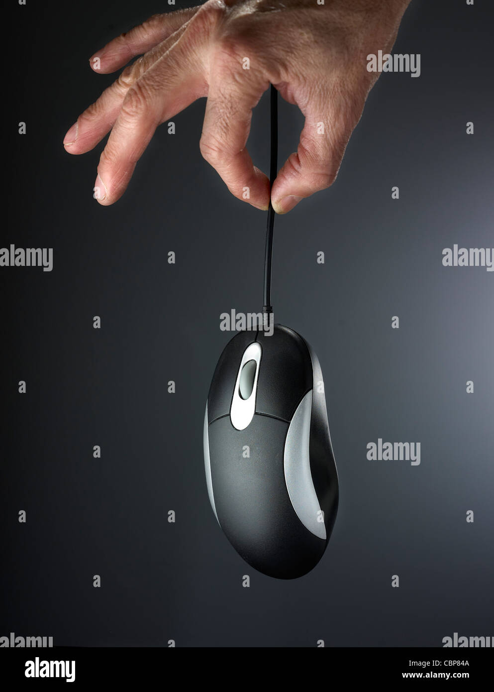 hand holding hanging computer mouse on dark graded neutral background ...