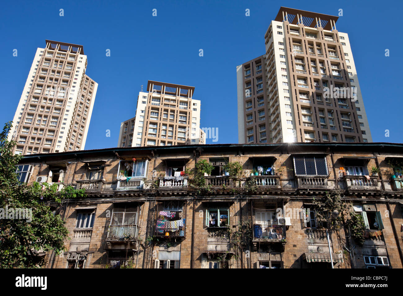 Old traditional tenement housing in shadow of new modern high rise apartment blocks at Mahalaxmi in Mumbai, India Stock Photo