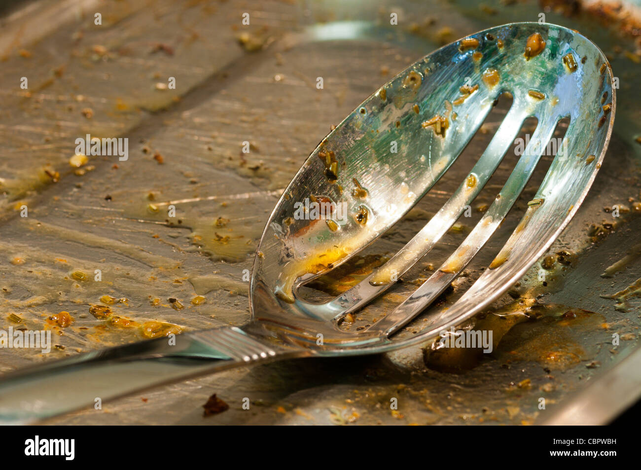 A greasy slotted serving spoon in a kitchen waiting to be washed up. Stock Photo