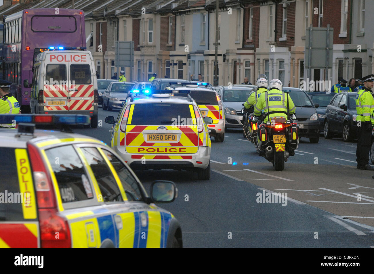 Multiple police vehicles with blue lights cross a city road junction during football match crowd control. Portsmouth Hampshire. Stock Photo