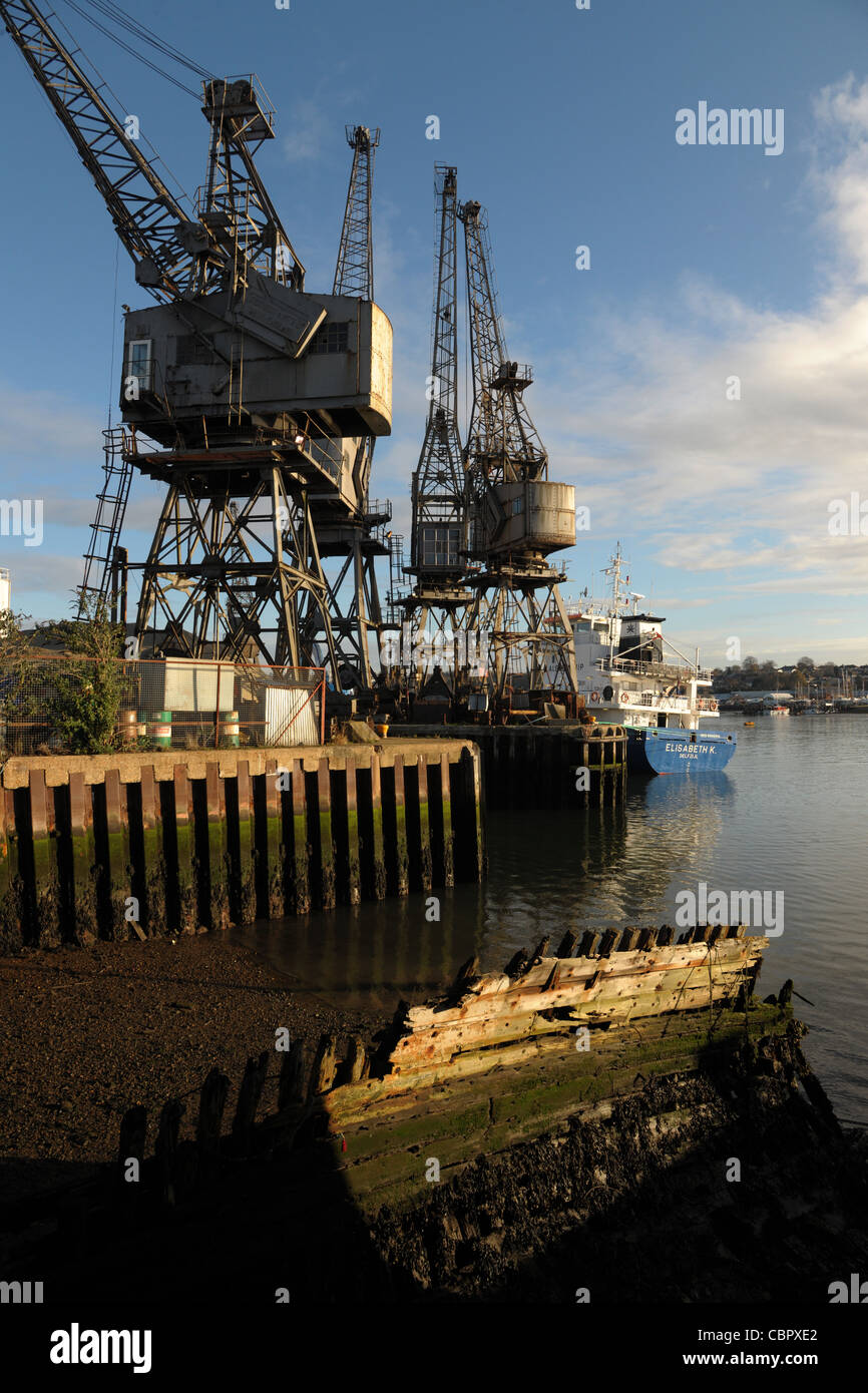 Old dockyard cranes on a harbour side jetty with an old rotting hulk in ...