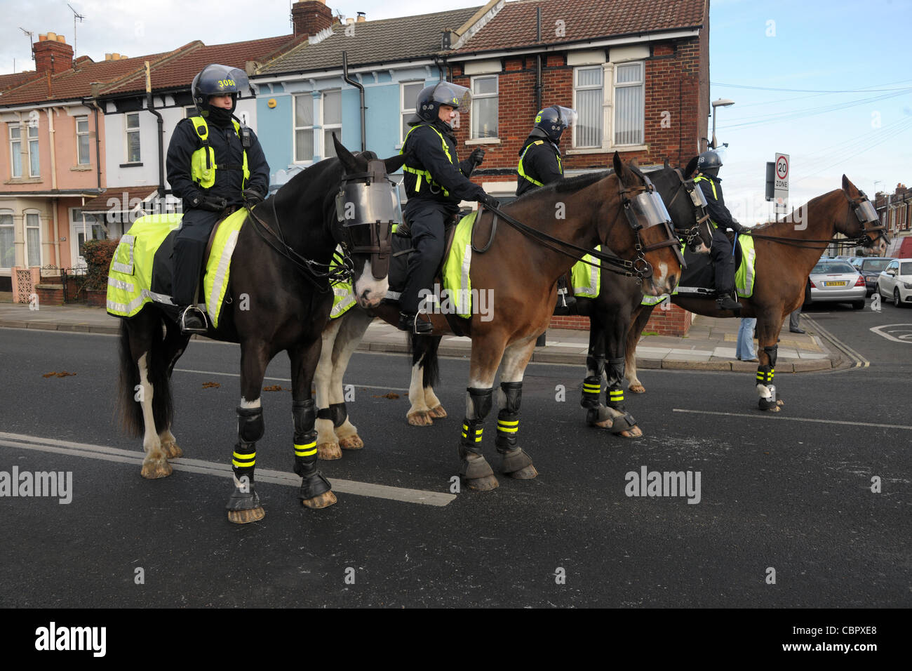 Mounted police officers and horses in protective riot dress block a road during a football match crowd control. Portsmouth Hants Stock Photo