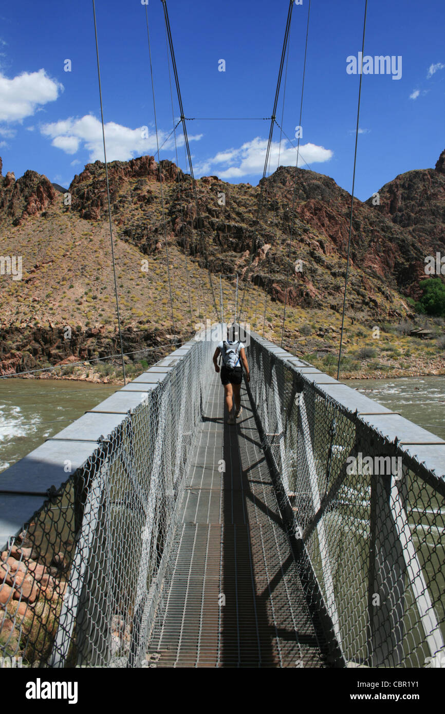 a woman hikes across silver bridge over the Colorado River at the bottom of the Grand Canyon, Arizona Stock Photo