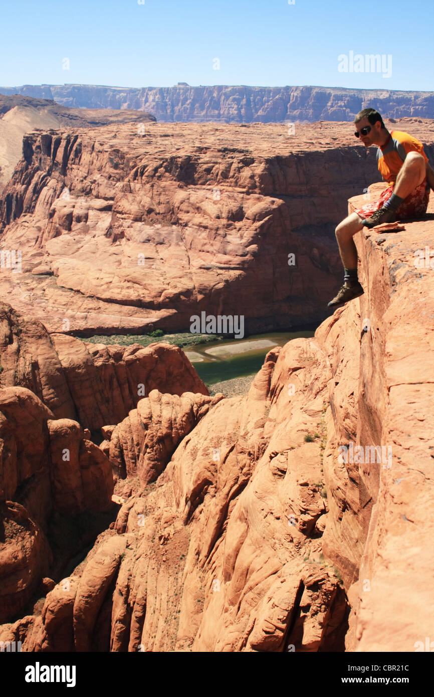 a man sits on the edge of a sandstone cliff overlooking Glen Canyon ...