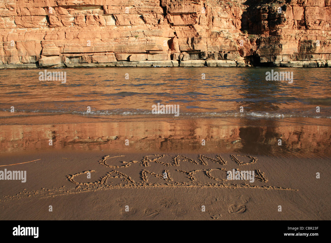 Grand Canyon written in the sand on a Colorado River bank beach across from a cliff Stock Photo