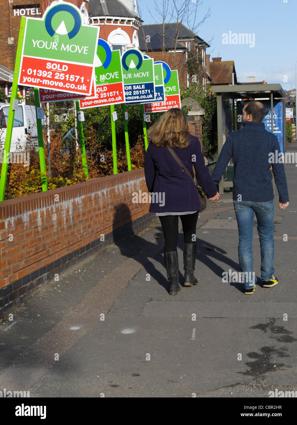 Young couple walking down road looking at House for sale and house sold signs on a street in central Exeter UK Stock Photo