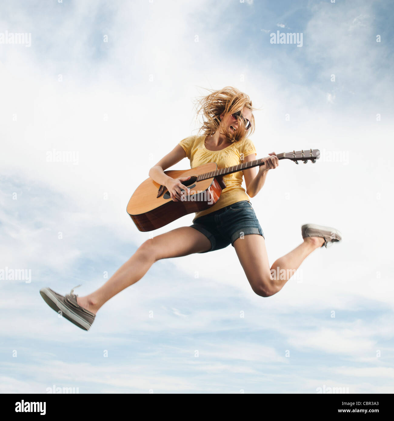 Caucasian woman jumping in mid-air playing guitar Stock Photo