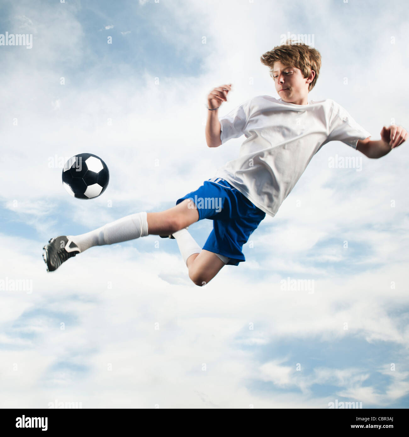 Caucasian teenager kicking soccer ball in mid-air Stock Photo