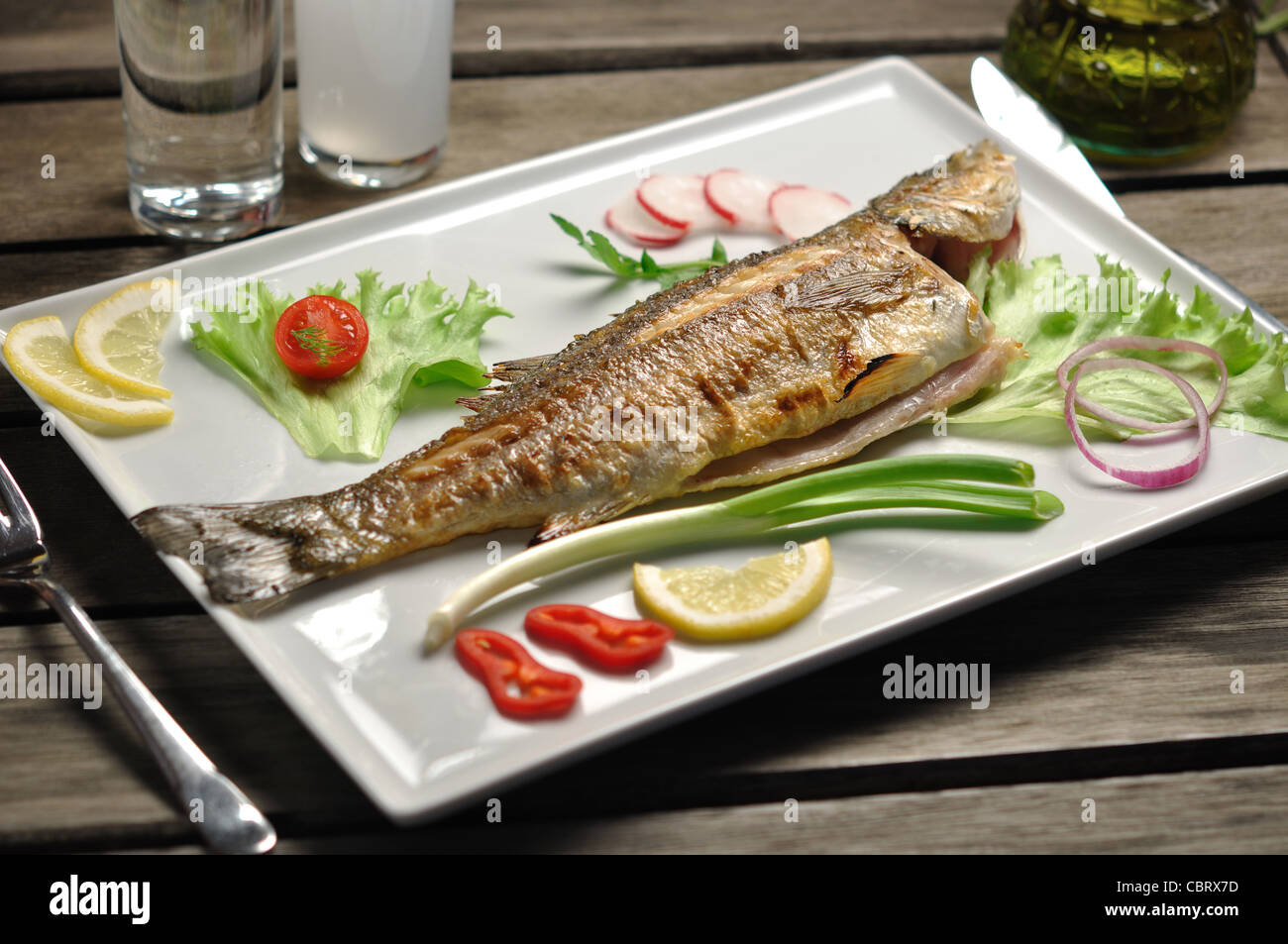 char grilled sea bass fish served with garnish and traditional Greek and Turkish alcohol rakı