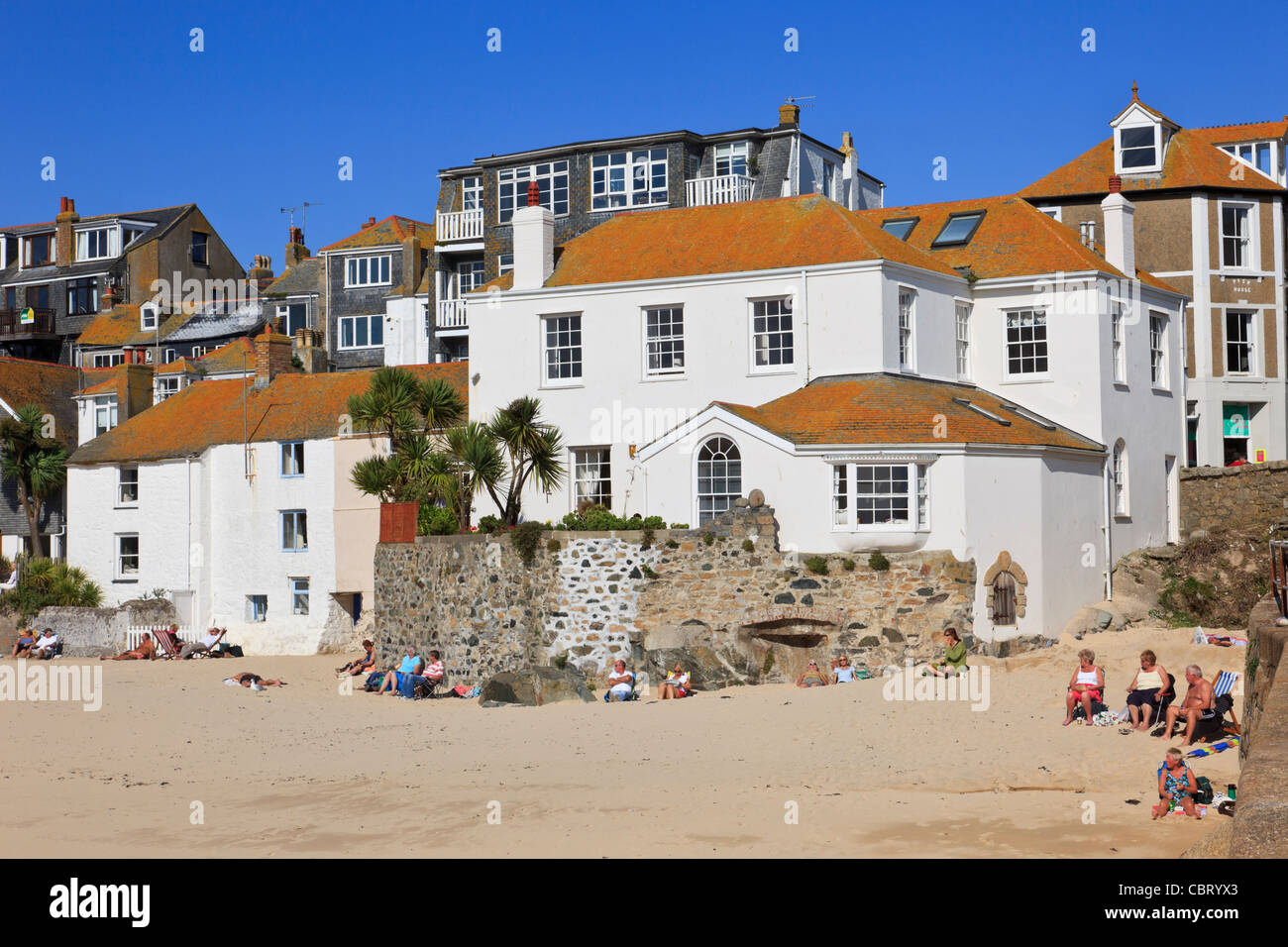 St Ives, Cornwall, England, UK. Traditional white buildings on seafront with people sitting on the sandy beach Stock Photo
