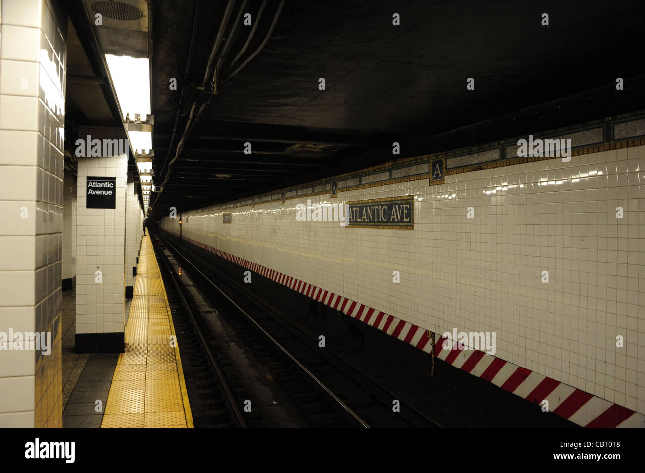 View of shiny white tiles deserted platform and rail lines, BM Brighton Line, Atlantic Avenue Subway Station, Brooklyn, New York Stock Photo