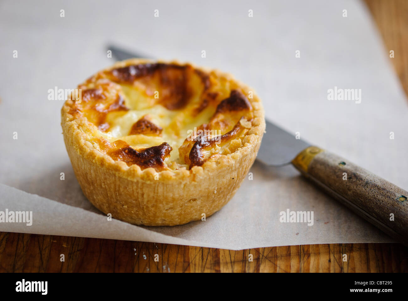 Little Quiche Lorraine on curled greaseproof paper with knife Stock Photo