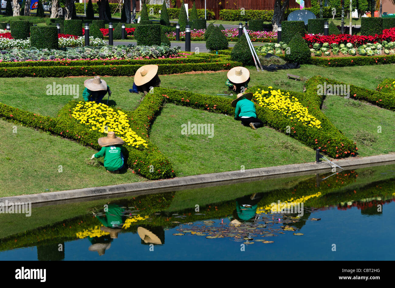 Pond reflects gardeners with huge floppy hats doing landscape maintenance at Royal Flora Ratchaphruek in Chiang Mai Thailand Stock Photo