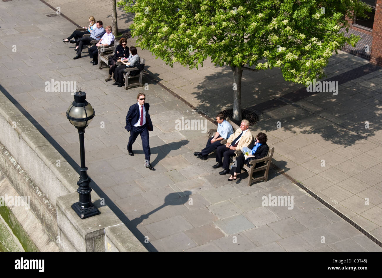 Lunchtime break for office workers on the Thames waterfront walkway below Millenium Bridge, Blackfriars, London, UK Stock Photo