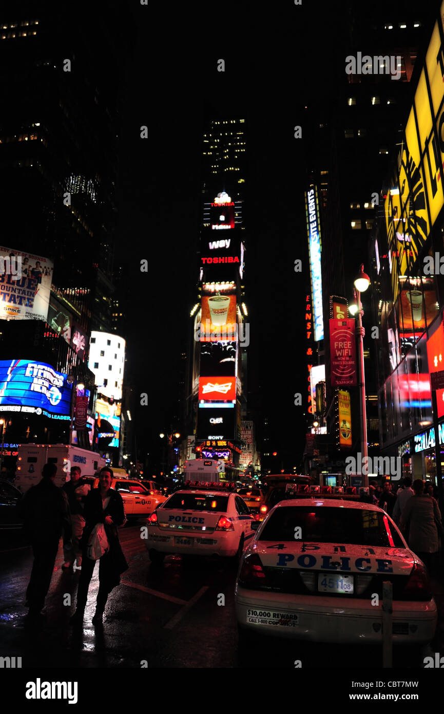 Wet tarmac night portrait people, neon billboards, two NYPD police cars parked, 7th Avenue, Broadway, Times Square, New York Stock Photo