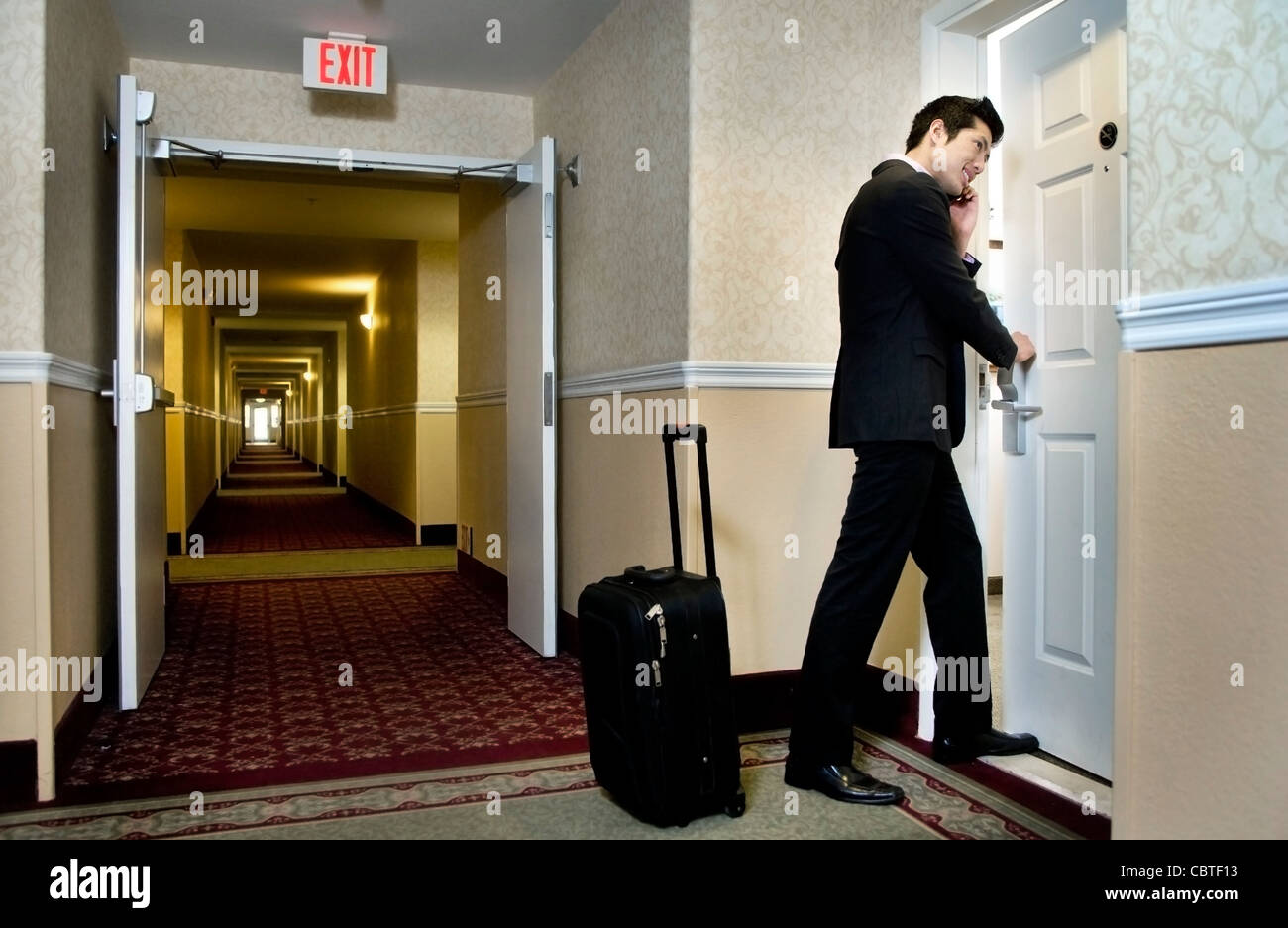 Asian businessman using cell phone and entering hotel room Stock Photo