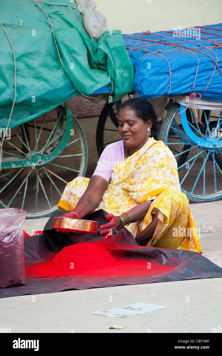 Indian woman sitting on an indian street sieving red coloured powder to remove bits . Puttaparthi, Andhra Pradesh, India Stock Photo