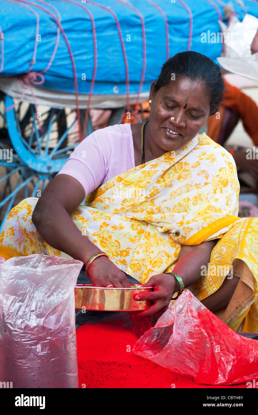 Indian woman sitting on an indian street sieving red coloured powder to remove bits . Puttaparthi, Andhra Pradesh, India Stock Photo