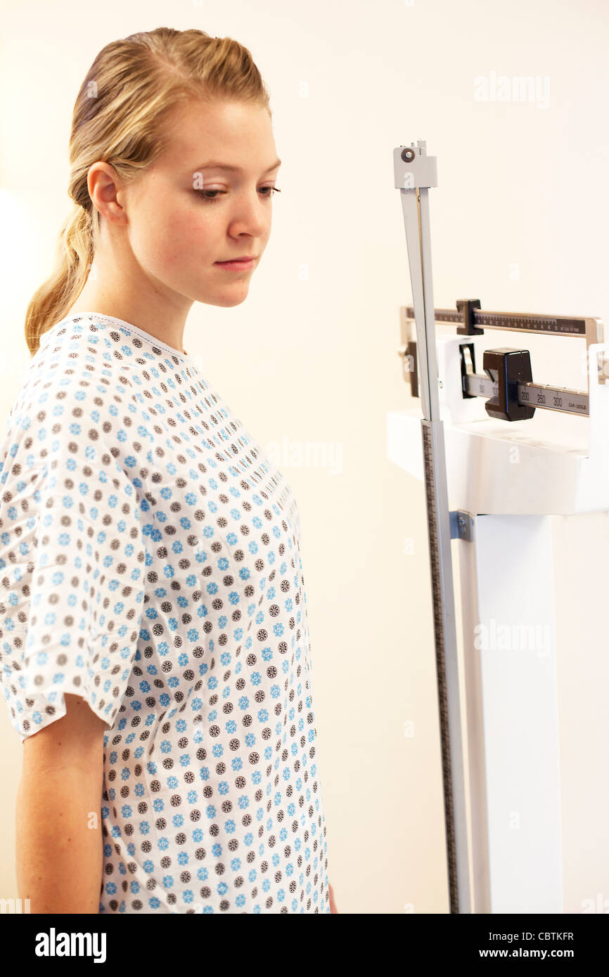 Young woman weighting herself at doctor's office scale. Stock Photo
