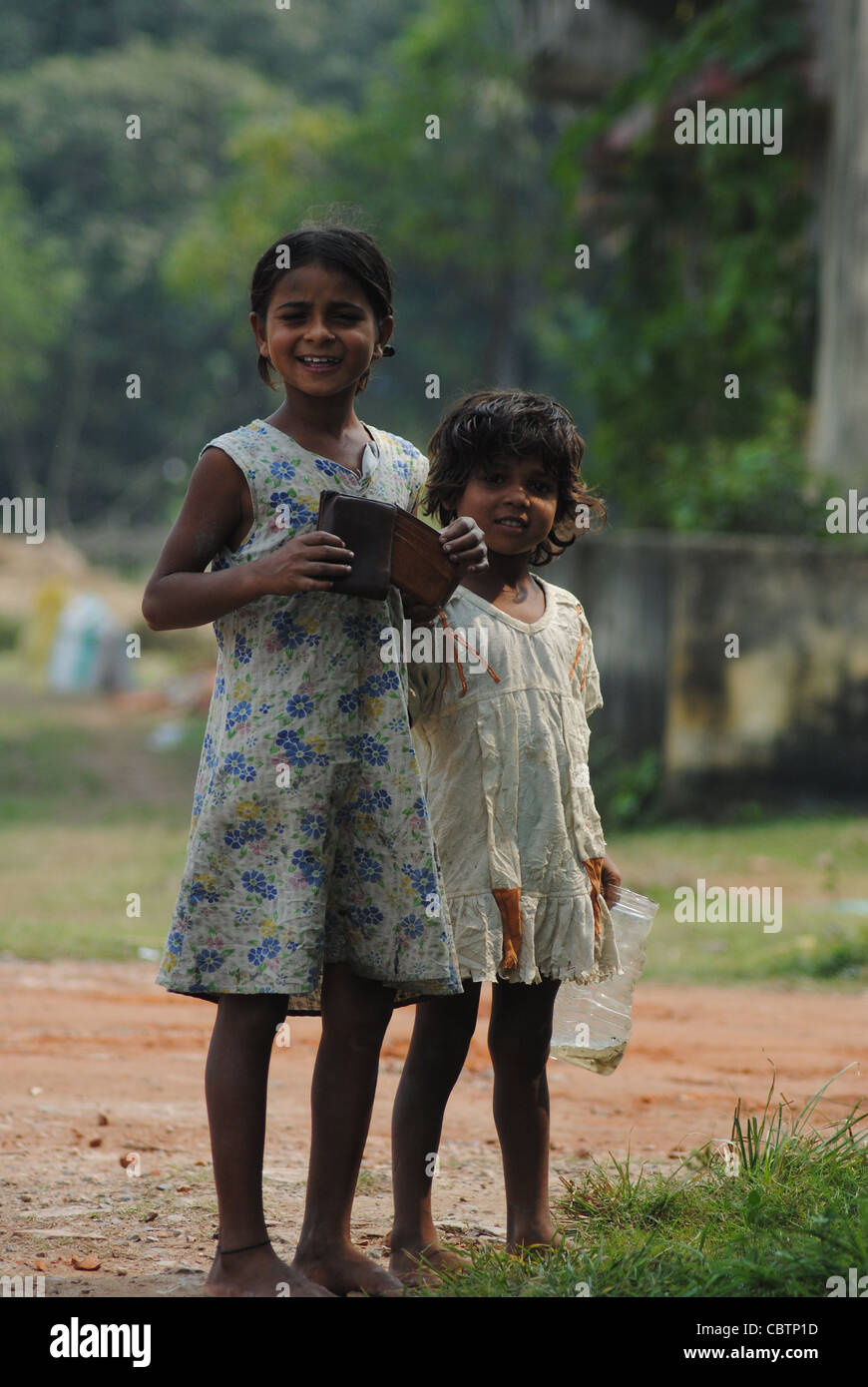 Two poor young girls faces the camera and smiles. Stock Photo