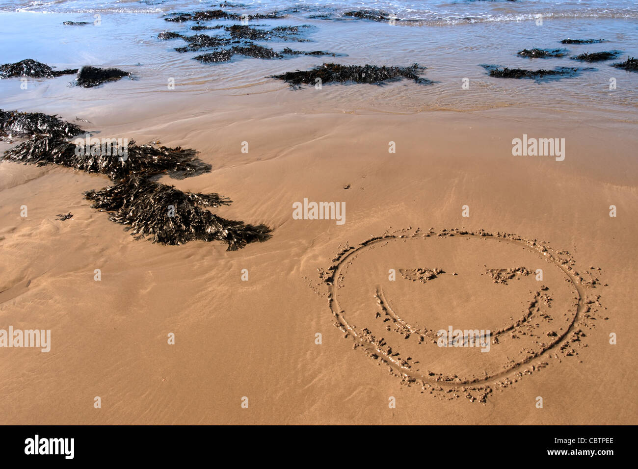 a smiley face icon inscribed on the beach with waves in the background on a hot sunny day Stock Photo