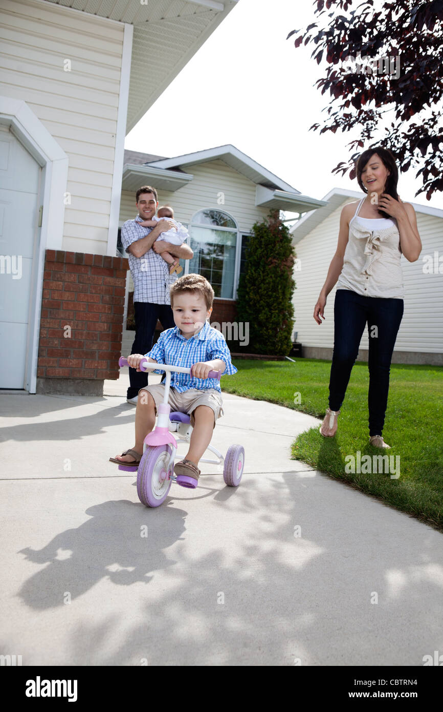 Little boy learning to ride tricycle while parents watch Stock Photo