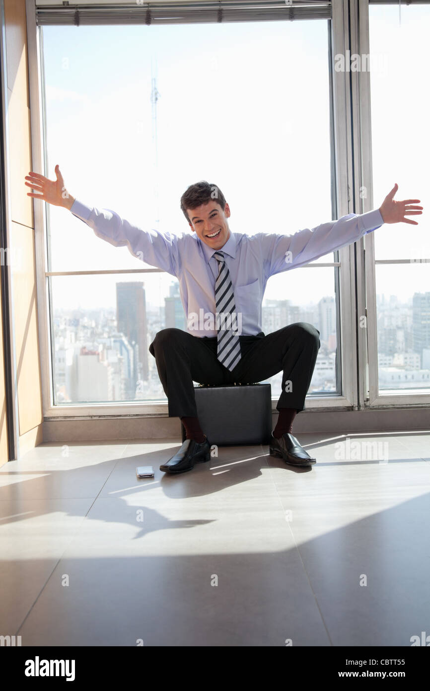 Portrait of excited male entrepreneur sitting on briefcase Stock Photo