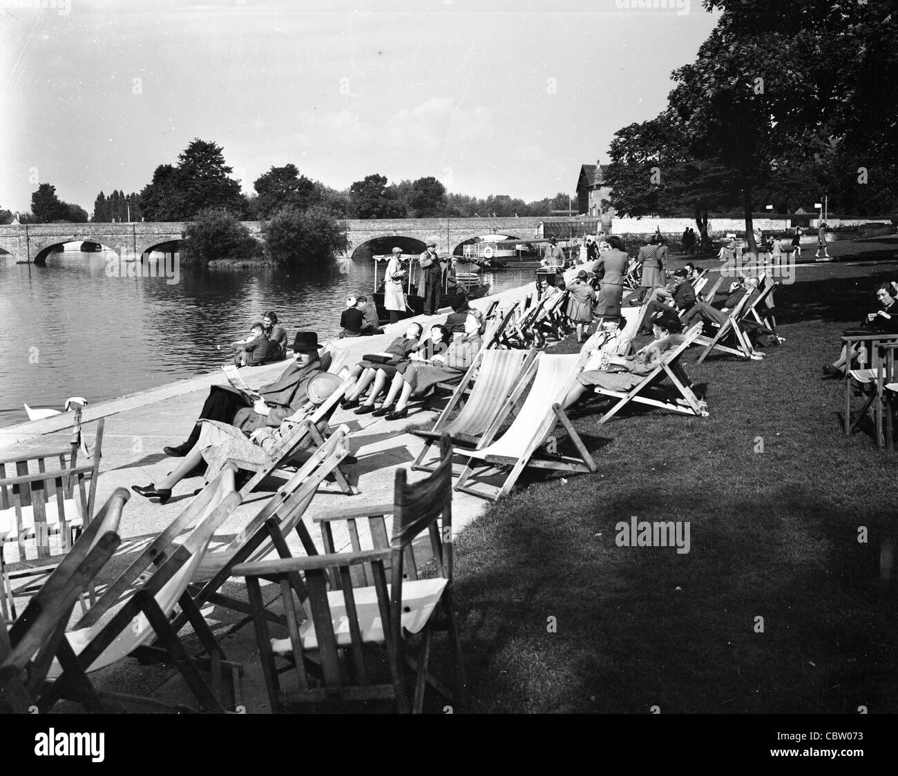 group of people relaxing in chairs next to river in WWII england UK britain folding furniture outdoors Stock Photo