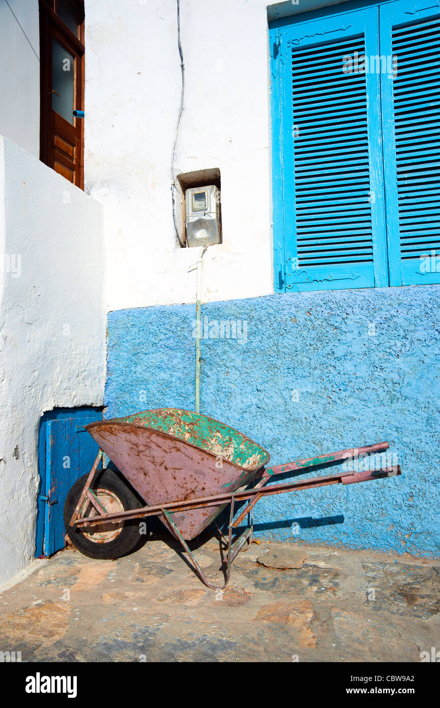 Still life of an old wheelbarrow against a light blue adobe wall. Taken on the Greek island of Amorgos. Stock Photo