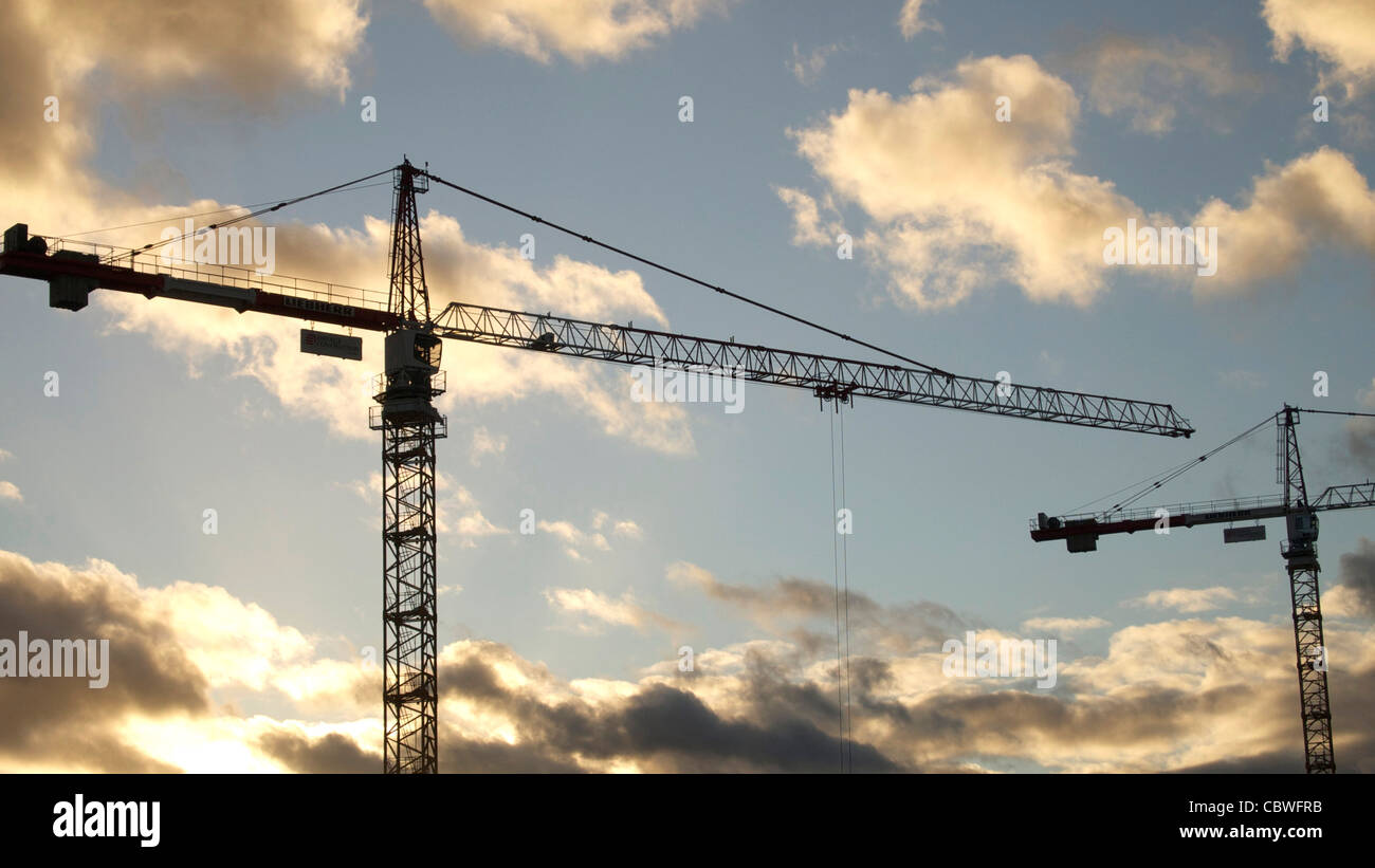 Construction cranes silhouetted against a sunset with clouds visible in ...