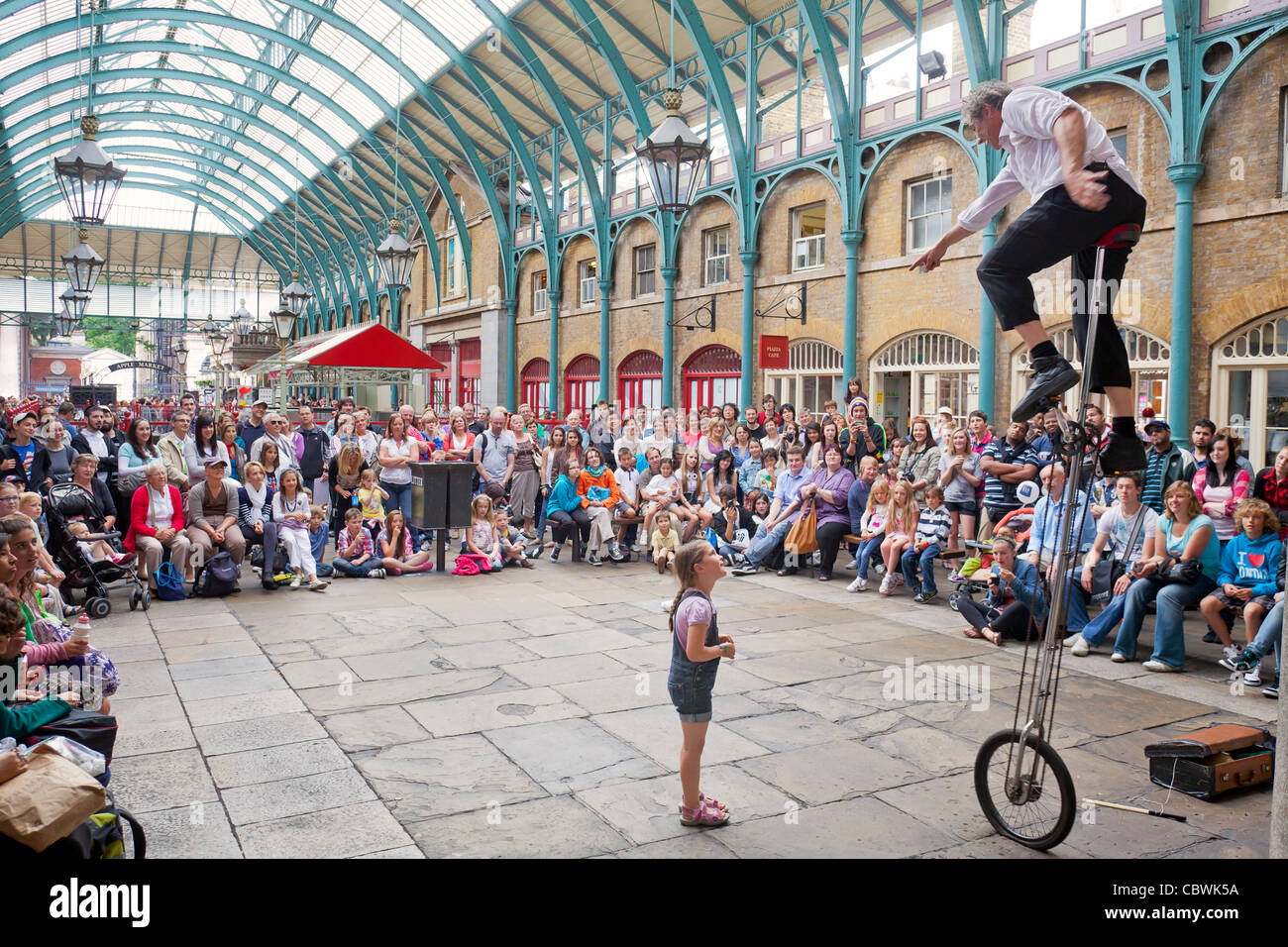 Tourists, shoppers and a street performer on a high bicycle with an audience at Covent Garden, London, England. Stock Photo