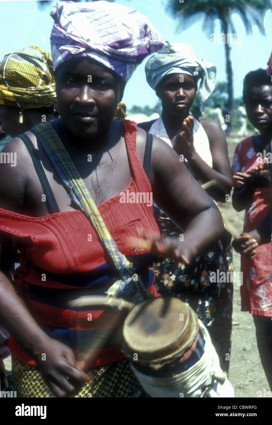 West African woman playing a drum in a rural village, Sierra Leone