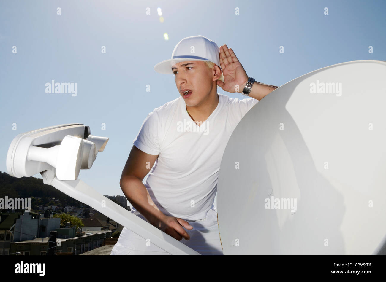 Young man wearing all white listening out next to a satellite dish and receiver Stock Photo