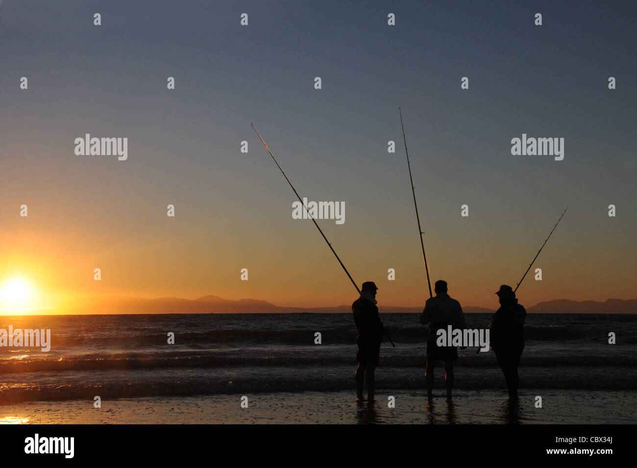 Three fishermen rod fishing in the sea from the beach at Strand, South Africa Stock Photo