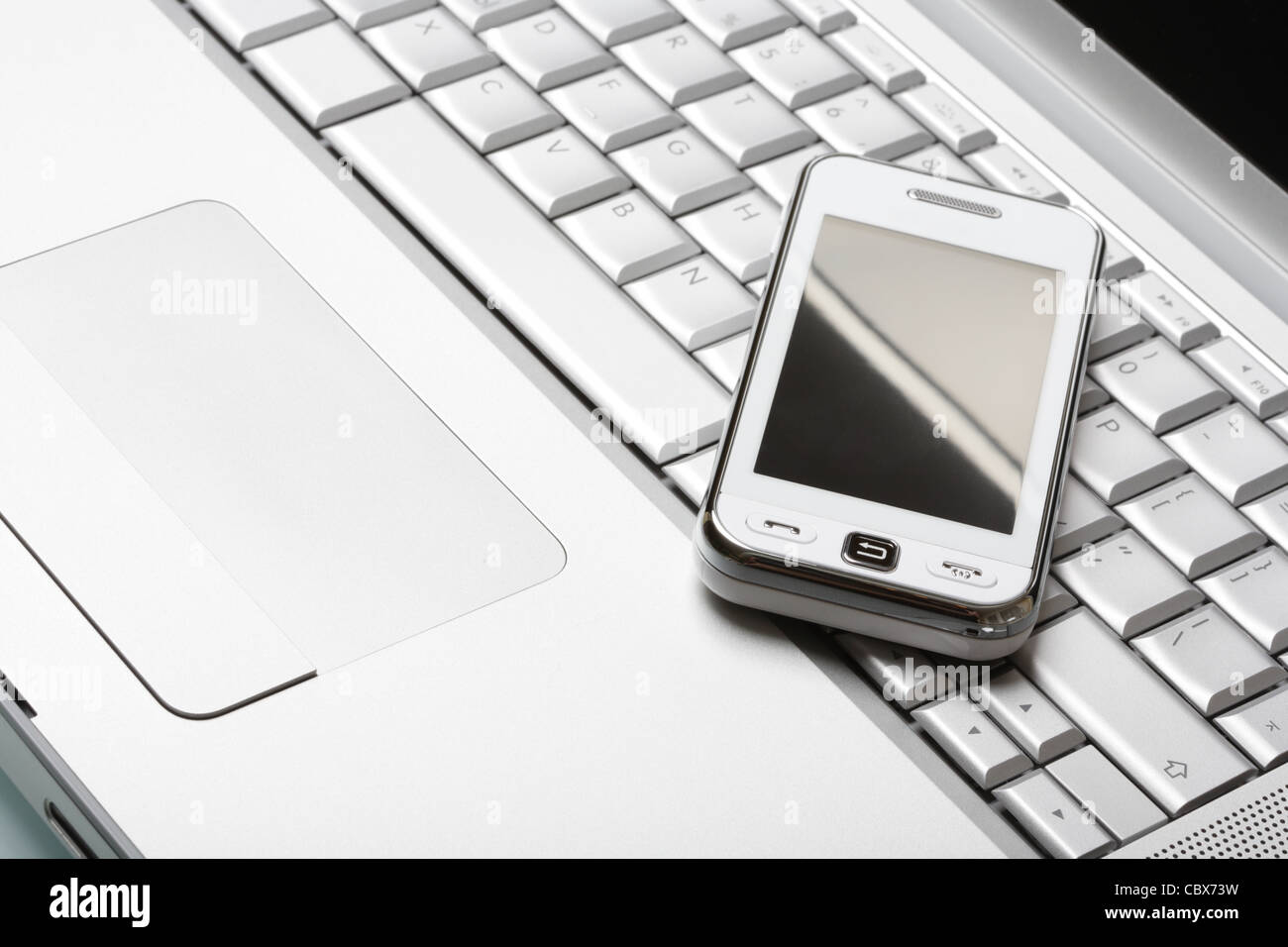 Modern communications concept. White touchscreen smartphone on a high-end aluminium laptop. Shallow DOF. Studio shot. Stock Photo